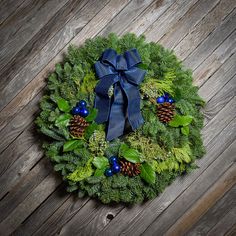 a christmas wreath with pine cones and evergreens on a wooden background, top view