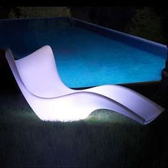 a white chair sitting next to a swimming pool in the grass at night with its lights on