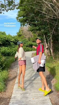 two people walking down a wooden walkway in the woods, one pointing at another person