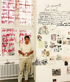 a man standing in front of a wall covered with red writing and pictures on it