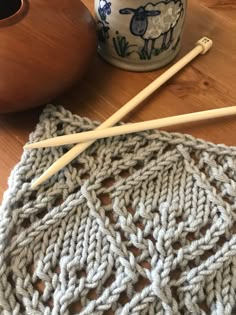 two knitting needles are laying on a table next to a knitted dishcloth and cup