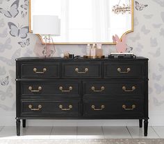 a black dresser with gold handles and drawers in front of a wallpapered background