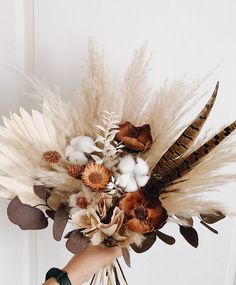 a woman holding a bouquet of dried flowers and feathers in front of a white door