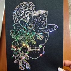 a hand holding up a card with a skull wearing a hat and flowers on it