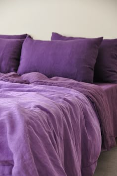 a bed covered in purple sheets and pillows