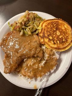 a white plate topped with meat and gravy next to some hash browns on top of rice