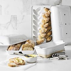 an assortment of breads and pastries in white containers on a marble countertop