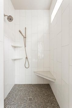 a walk in shower sitting next to a white tiled wall and floor with shelves on each side