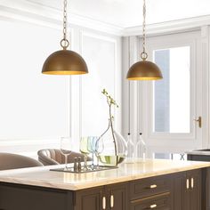 two lights hanging over a kitchen island with wine glasses and flowers in vases on it