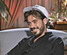 a man wearing a hat sitting in a chair with his arms crossed and smiling at the camera