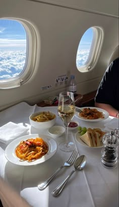 a man sitting at an airplane table with food and wine in front of the window