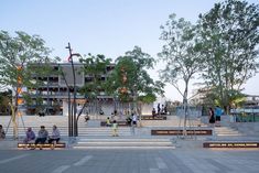 several people sitting on benches in front of a building with stairs and trees around it