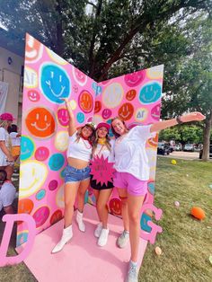 two girls standing in front of a giant pink sign with smiley faces on it's face