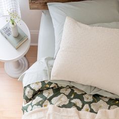 a bed with white flowers on it and a green comforter next to a small table