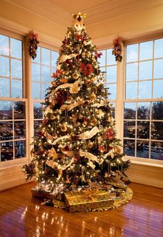 a decorated christmas tree in a room with large windows and wooden flooring on the side