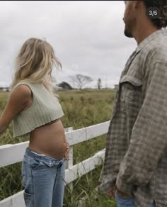 a man and woman standing in front of a white fence looking at each other with their backs to the camera