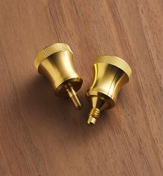 two gold colored metal knobs on a wooden surface, one has a screw in the middle