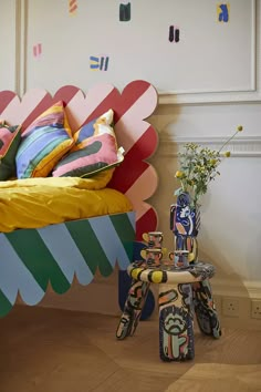 a bed with colorful pillows on top of it next to a small table and flower vase