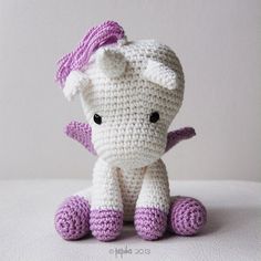 a crocheted white and purple stuffed animal sitting on top of a table next to a wall