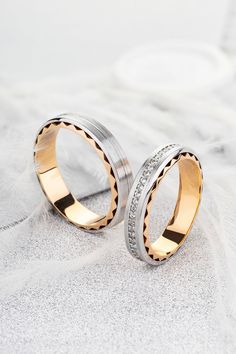 two gold and silver wedding rings with diamonds on top of each other in front of a white background