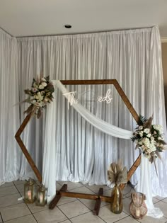 a decorated wedding arch with flowers and candles on the floor in front of a white curtain