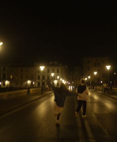 two people are running down the street at night with their arms in the air and one person is holding an umbrella