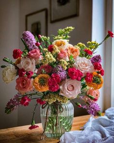 a vase filled with lots of different colored flowers on top of a wooden table next to a window