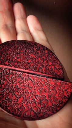 a hand holding a red piece of leather in it's palm, which is shaped like a leaf