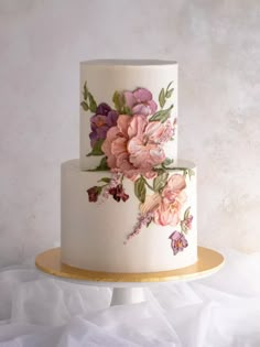 a three tiered white cake with pink and purple flowers painted on the top layer