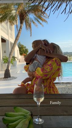 a woman holding a child in her arms next to a glass of wine and bananas