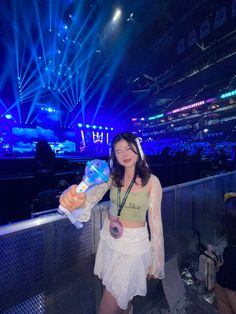 a woman standing in front of a stage holding a water bottle and wearing a white skirt