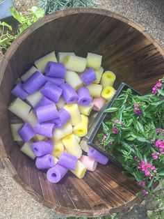 a wooden bowl filled with purple and yellow food next to some flowers on the ground