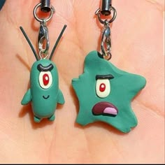 two green cartoon characters are attached to small key chains on a person's hand