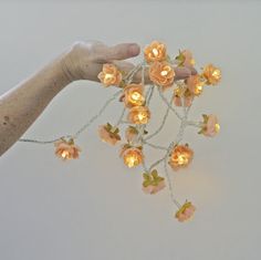 a hand is holding a string with flowers on it and lights attached to the strings