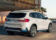 a white bmw suv is parked in front of a building with palm trees behind it