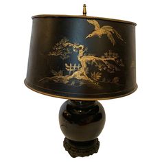 a table lamp with a black shade and gold decoration on the bottom, sitting on a white surface