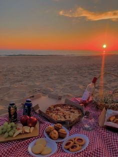 a picnic on the beach at sunset with pizza, fruit and beer in front of it