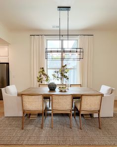 a dining room table with four chairs and a vase on top of it in front of a window