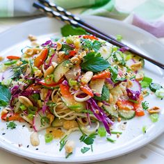 a white plate topped with noodles and veggies next to two chopsticks