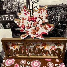 a sign that is sitting on top of a bench in front of a building with autumn leaves painted on it