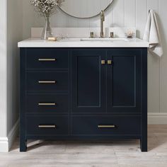 a white sink sitting under a mirror next to a blue cabinet with gold handles and drawers