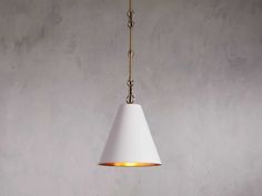 a white lamp hanging from a gold chain on a gray wall with concrete flooring