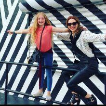 two women posing for the camera in front of a wall with black and white stripes