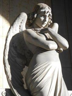 an angel statue sitting on top of a white wall next to a building with its arms crossed