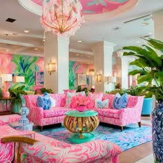 a living room filled with pink couches and lots of green plants in front of a chandelier