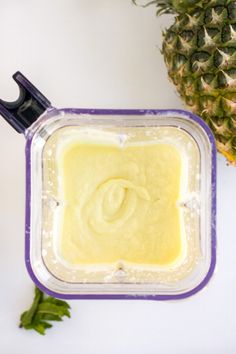 a blender filled with yellow liquid next to a pineapple on a white surface