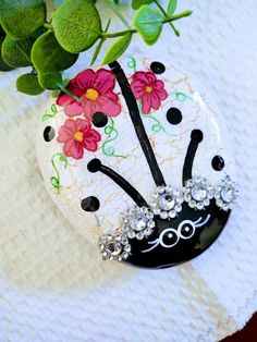 a black and white lady bug brooch with pink flowers on it's head