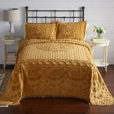 a bed with yellow comforter and pillows on top of it, next to a night stand