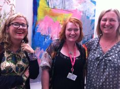 three women standing next to each other in front of paintings