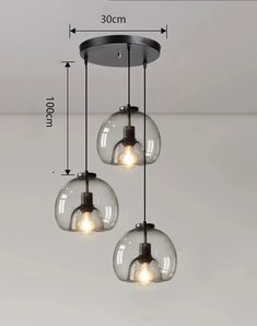 three clear glass globes hanging from the ceiling, with measurements for each light bulb